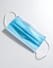 Overhead shot of a light-blue surgical mask with white ear loops
