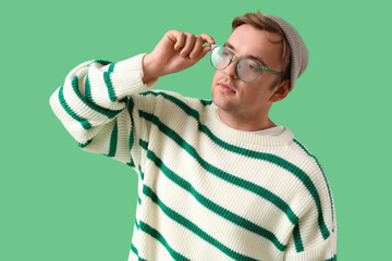 Stylish young man in striped sweater with eyeglasses on green background