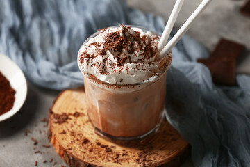 Glass of cold cocoa drink with whipped cream on grey background, closeup