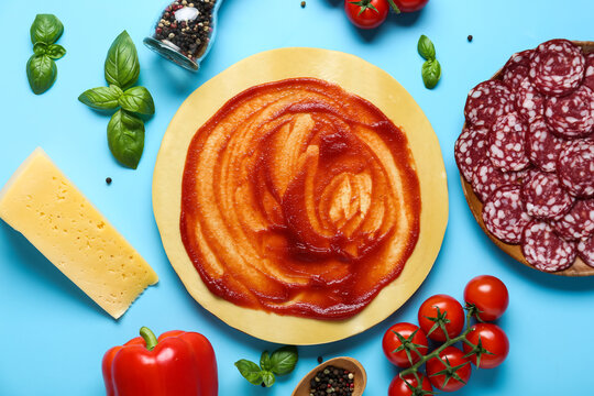 Pizza dough with tasty tomato sauce and ingredients on blue background - Powered by Adobe