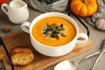 Pot of delicious pumpkin cream soup with seeds and herbs on grey grunge background, closeup