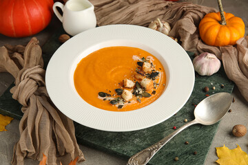 Plate of tasty pumpkin cream soup on grey grunge background, closeup
