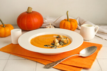Plate of delicious pumpkin cream soup with seeds and croutons on white tile table, closeup