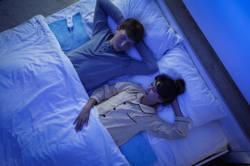 Young couple sleeping on electric heating pad in bedroom at night, top view