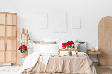 Interior of bedroom with paintings, tasty breakfast and Christmas plant poinsettia