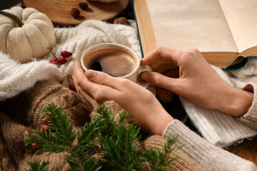 Female hands with mug of tasty coffee, sweaters and fir tree branches on wooden background, closeup