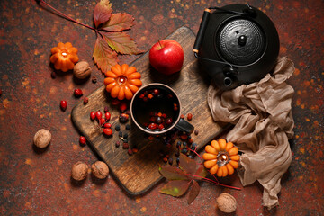 Composition with mug of hot berry tea, teapot, burning candles and autumn decor on brown grunge...