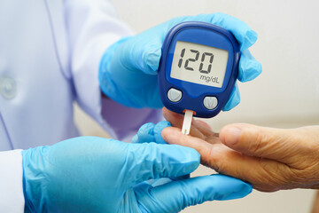 Asian doctor using digital glucose meter for check sample blood sugar level to treatment diabetes.