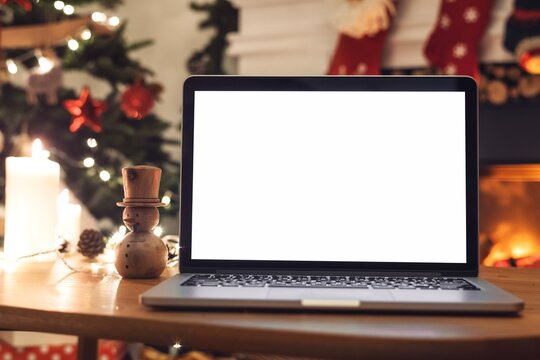 Cozy holiday scene with a laptop screen mockup on a wooden table. Christmas decorations, laptop, and festive lights create a warm, inviting atmosphere. Laptop and holiday decor. - Powered by Adobe