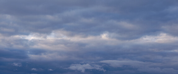 Fluffy clouds with shades of grey and blue hues fill the sky, giving the impression of an impending rainstorm, as the last light of the day filters through