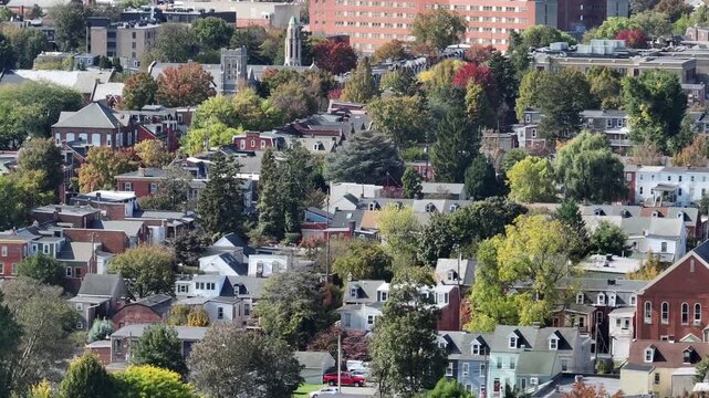 Row of houses and townhouses with downtown and church in background. Aerial wide shot. Multi colored trees In autumn season. Sunny day in historic neighborhood of america.