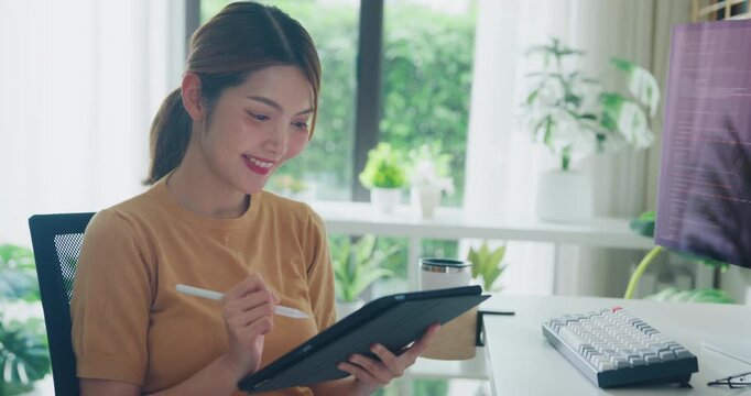Young adult Asia female freelance write code on tablet while work prompt AI bot IT app smart program nomad, video game, terminal coding, user interface, data center on desktop computer at home office.