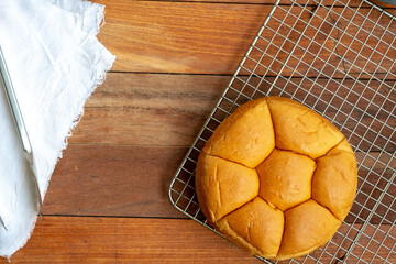 A top-down view of a segmented bread roll on a metal cooling rack. A white cloth is to the left, all on a wooden table.