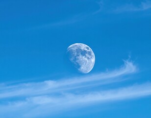 Clear blue sky with crescent moon and wispy clouds scattered around