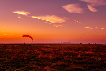 Wenn der Himmel Feuer fängt und die Welt in flüssiges Gold taucht, tanzt ein roter Schirm am Horizont. Ein Gleitschirmflieger schwebt zwischen Erde und Äther, gefangen in diesem Moment, wo der Tag sei
