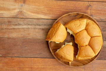 A top-down view of a segmented bread roll on a round wooden plate, with two pieces cut and separated. The plate rests on a wooden table, providing copy space to the left.