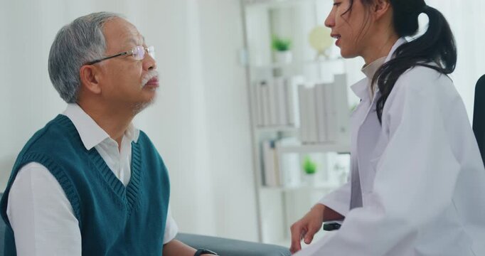 Young Asia female doctor with mature male patient check throat diagnosis and consultation for examination healthcare on sofa in clinic office. Otolaryngologist for thyroid health, pain and infection.