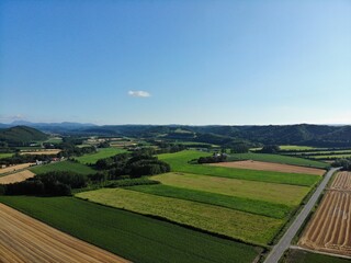 Fototapeta premium Aerial Panorama of Patchwork Farmland, Rolling Hills and Country Road in Hokkaido, Japan