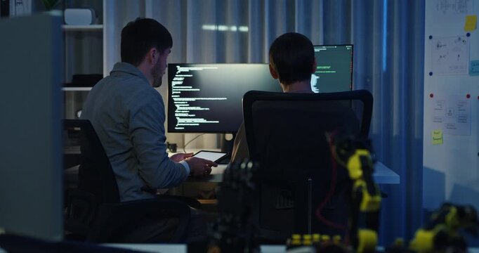 Team adult male engineer collaborate on robotic hand project using AI code solutions machine learning at tech workspace night. Artificial intelligence interface, collaboration prototype development.