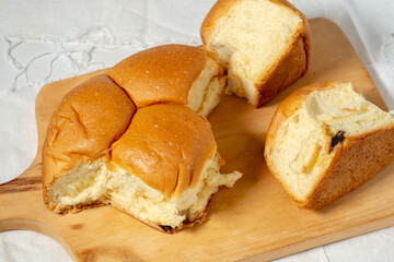 A close-up of a soft, golden-brown bread roll torn into several pieces, revealing the fluffy interior, all placed on a wooden cutting board over a white cloth.