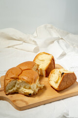 Torn pieces of a soft, golden-brown bread roll are arranged on a wooden cutting board, revealing the fluffy interior, all set against a white cloth and plain white background with copy space.