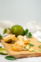 Peeled orange segments are stacked on a wooden cutting board. Green peels, leaves, and a halved orange are scattered nearby, with a shallow depth of field.