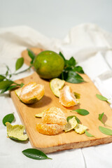 Peeled orange segments are stacked on a wooden cutting board. Green peels, leaves, and a halved orange are scattered nearby, with a shallow depth of field.