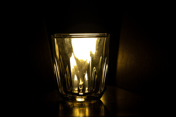 A faceted drinking glass is illuminated from behind by a warm, golden light against a solid black background.