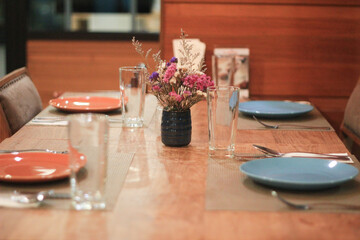 Cozy empty restaurant table setting ready for romantic dinner. indoor dining arrangement with flower vase on wooden table creates warm, inviting atmosphere