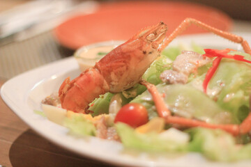 Delicious cooked prawn on fresh seafood salad with tomato. This gourmet meal and healthy appetizer served on white plate evokes an appetizing and tasty dining experience