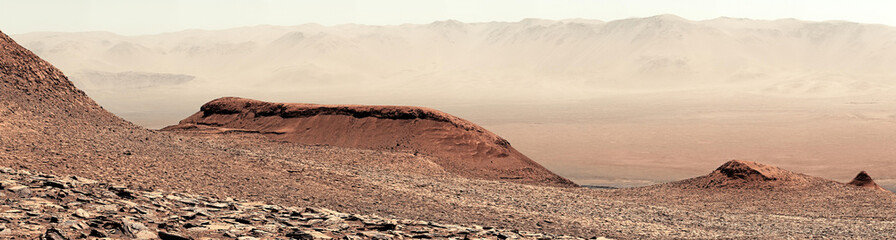 An arid, rocky, and expansive martian landscape with hazy distant peaks.