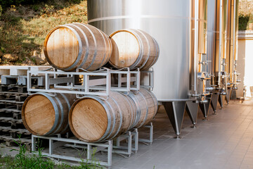 Modern stainless steel wine fermentation tank and traditional oak barrels in an outdoor winery setup under natural daylight
