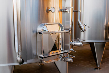 Industrial stainless steel fermentation tanks with valves, pressure gauge, and sight glass in a modern brewery or winery production facility interior