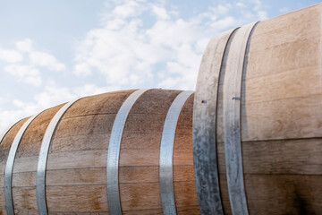 Close-up of oak wine barrels with metal hoops outdoors under blue sky with clouds, winery storage, traditional aging process