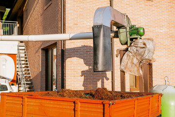 Industrial grape pomace extraction system at a winery with automated pipe loading into orange trailer for composting or biofuel use, captured in evening sunlight