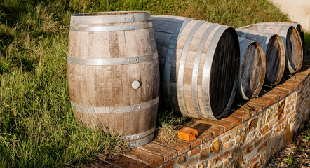 Aged wooden barrels outdoors on a rustic brick wall in a countryside vineyard, used for traditional wine fermentation and aging under natural sunlight