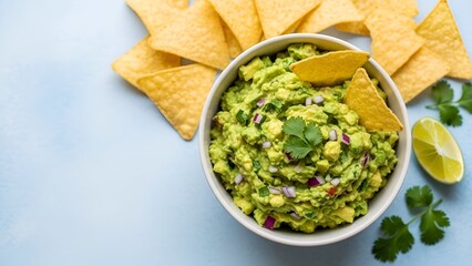 Delicious Guacamole Bowl Surrounded by Tortilla Chips and Lime on a Light Blue Surface