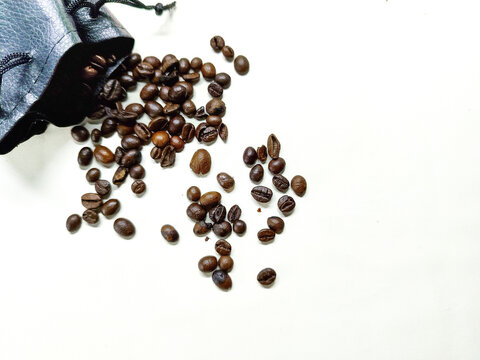 Close-up of roasted coffee beans spilled from a black pouch on a white surface, showcasing the rich aroma and texture of premium coffee
