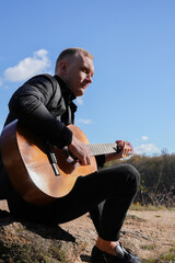 Portrait of smiling caucasian artist plays wooden acoustic guitar in autumnal park. Young songwriter plays string musical instrument hobby outside in nature fall time. Audio music healing in natural