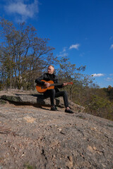 Blonde man playing string guitar outdoors in autumn forest. Concept of sound therapy, mental health and wellness rituals. Calmness tranquility audio-sensory practices. Aura farming energy holistic