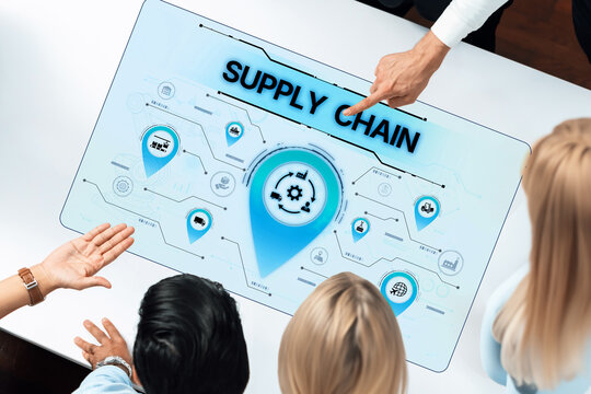 A group of diverse professionals gathers around a digital interface illustrating supply chain management. The visualization highlights connectivity and strategies for operational improvement. Trope