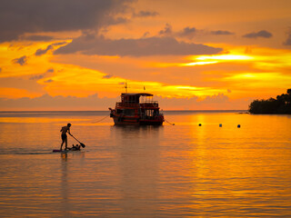 Silhouette of fishing boat and a man paddleboarding on the sea at sunset, Thailand