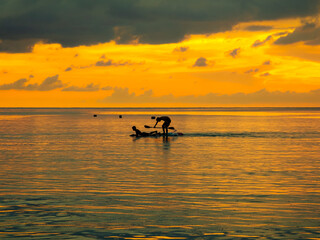 Silhouette of fishing boat and a man paddleboarding on the sea at sunset, Thailand