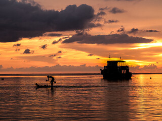 Silhouette of fishing boat and a man paddleboarding on the sea at sunset, Thailand