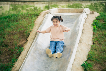 Happy young girl enjoying slide outdoors in a park, playful moments on a sunny day, childhood joy,...