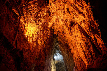 A cave with orange walls and a light shining on it. The light is coming from the top of the cave