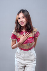 Smiling Asian woman showing gratitude with hand on chest in casual outfit