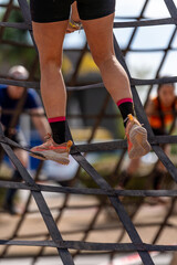 Close-up of the legs and shoes of a female athlete climbing a steep rope obstacle during a fitness race