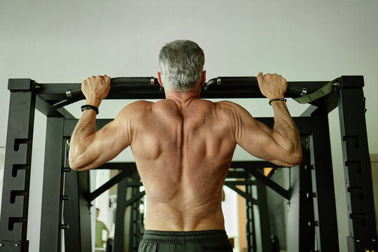 Middle Aged Man Exercising by Performing Pull Ups in Gym Setting