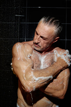 Middle Aged Man Washing Body in Shower with Serious Expression